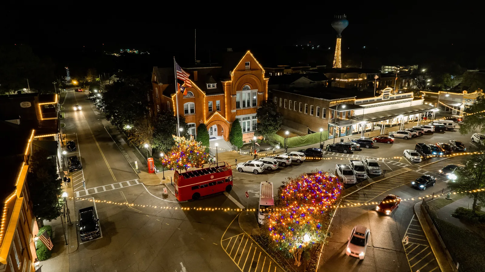 Holiday lights outline City Hall and the shops on the Square in Oxford, with the water tower lit up behind.