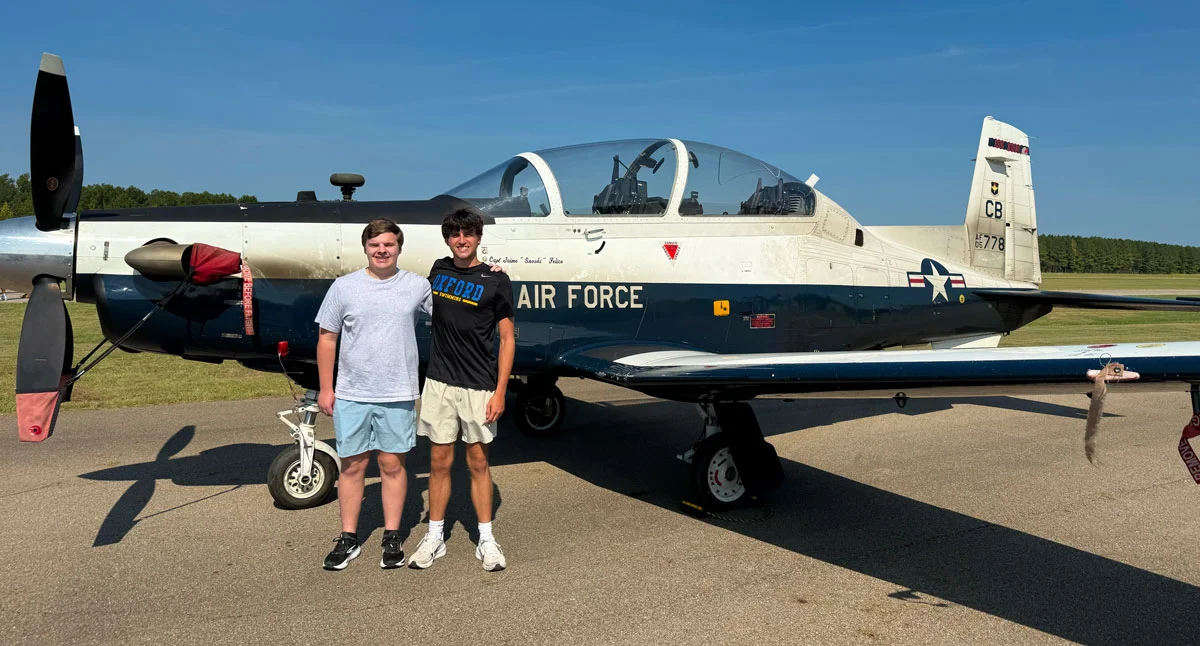 The two Oxford High School seniors behind Oxford Aerial Imaging beside an Air Force training plane at Aviation Day at Monroe County Airport in Aberdeen.